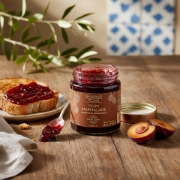A rustic Greek breakfast table with Navarino Icons Plum Marmalade on toasted bread, fresh plums, and an olive branch, highlighting its artisanal quality