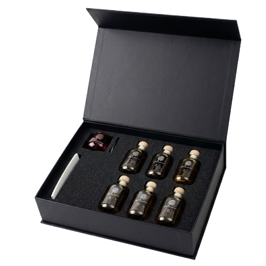 Open elenianna olive oil tasting kit showing six numbered sample bottles, a red tasting glass, and a tasting guide in a foam insert