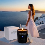 The Aurean Nox luxury candle placed on a balcony overlooking the iconic Oia sunset and blue-domed churches in Santorini, Greece.